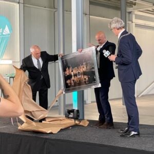 Three men in suits, on stage, presenting a piece of art at the opening of the Applied Medical sterilization facility.