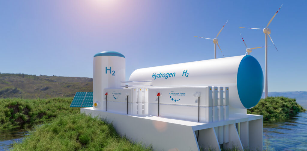 Hydrogen storage. Large white cylinders in a green field and next to water, with wind mills and solar panels in the background. Bright blue sky above. 