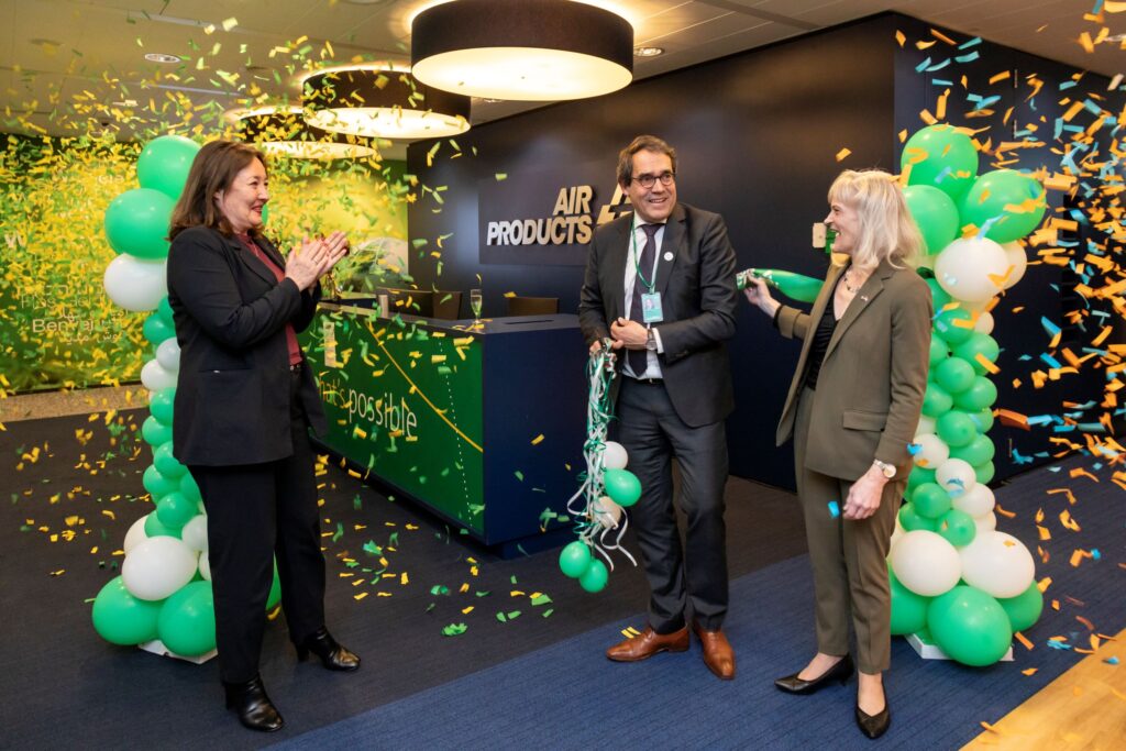 Two women and one man in suits celebrate the opening of a new office in front of balloons and confetti.