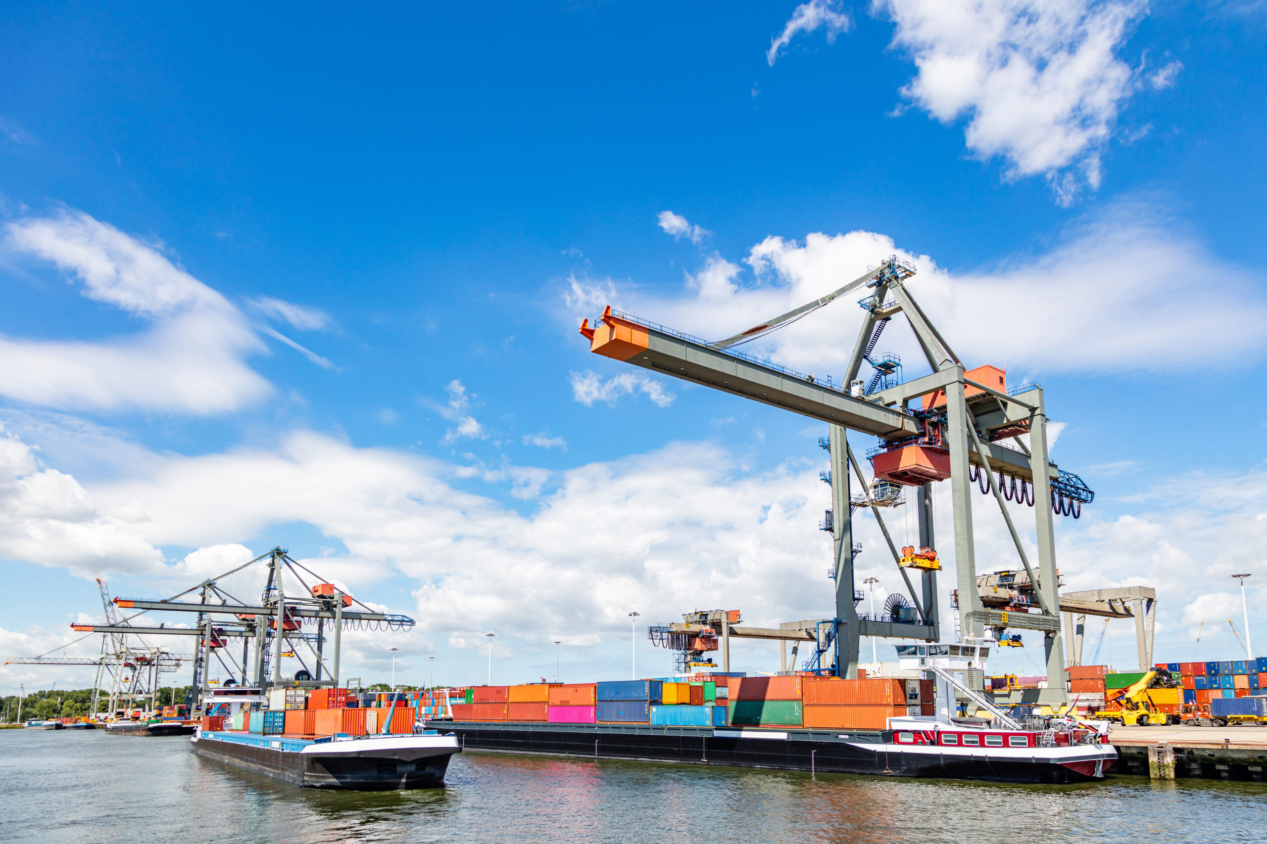 Shipping cargo being loaded by a crane on the international commercial harbor of Rotterdam, Netherlands, on a sunny day with blue skies and a few white clouds — Invest in Holland.