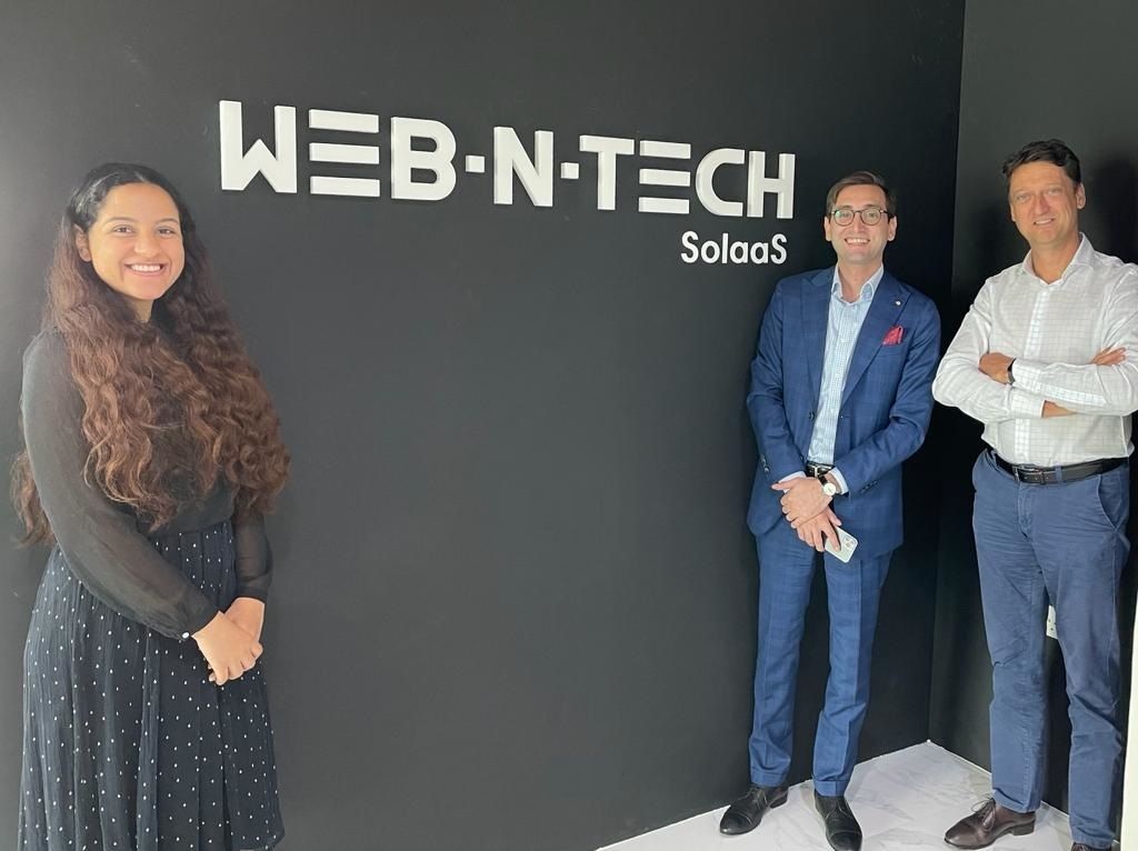 A woman and two men stand on either side of a wall displaying the word WebNTech - Invest in Hollad.
