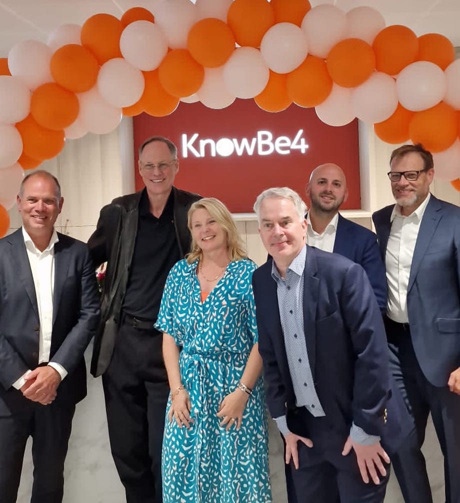 A group of business people in front of a orange and white balloon arch at the KnowBe4 office opening.