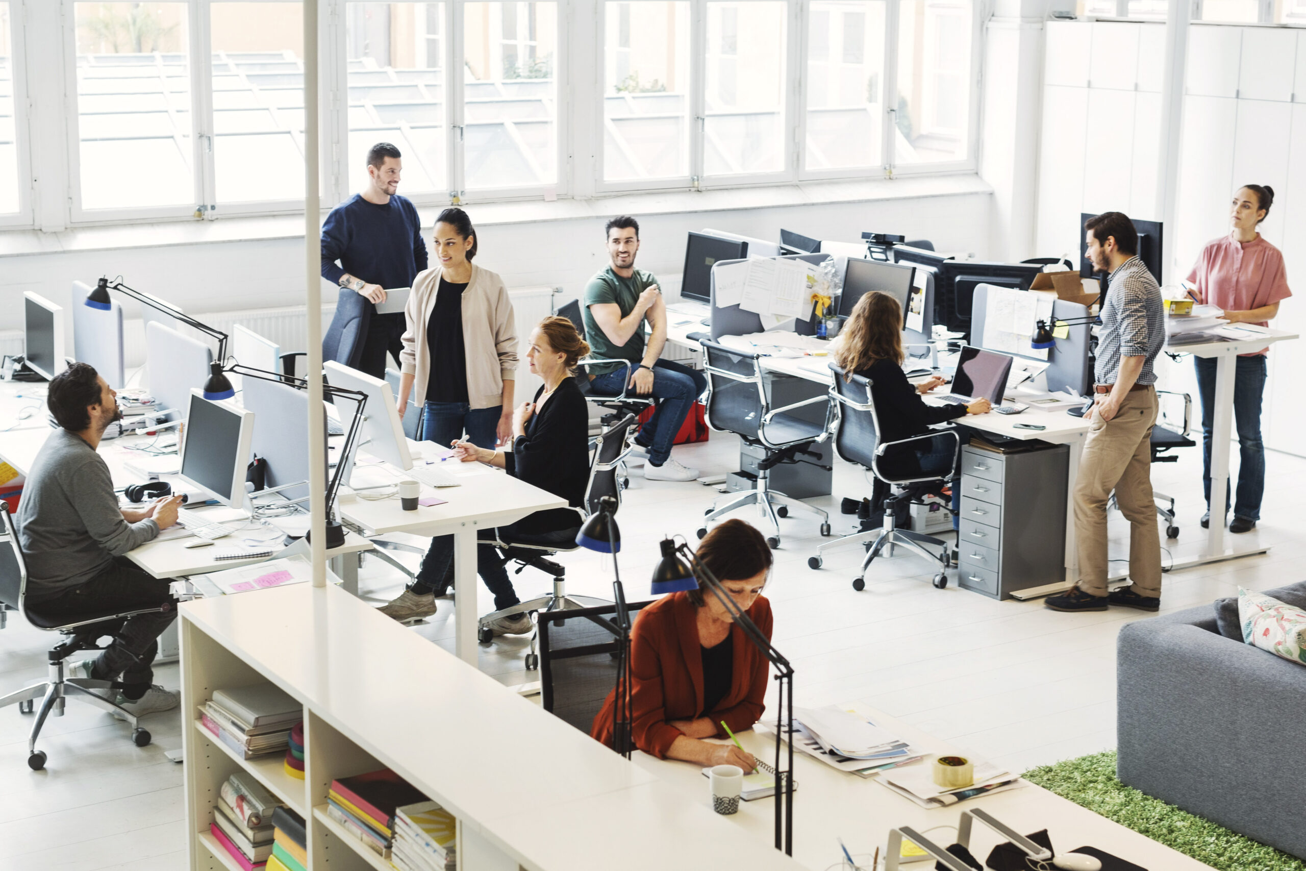 High angle view of business people working in a modern office. Some sit at a long, white desk, others stand—Invest in Holland.