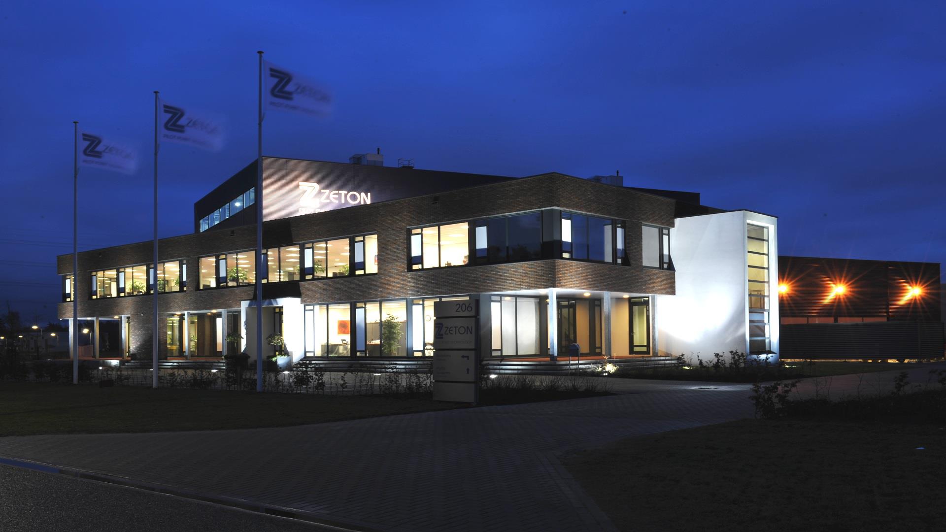 A night view of Zeton's facility in Enschede. Lights illuminate the building from within — Invest in Holland