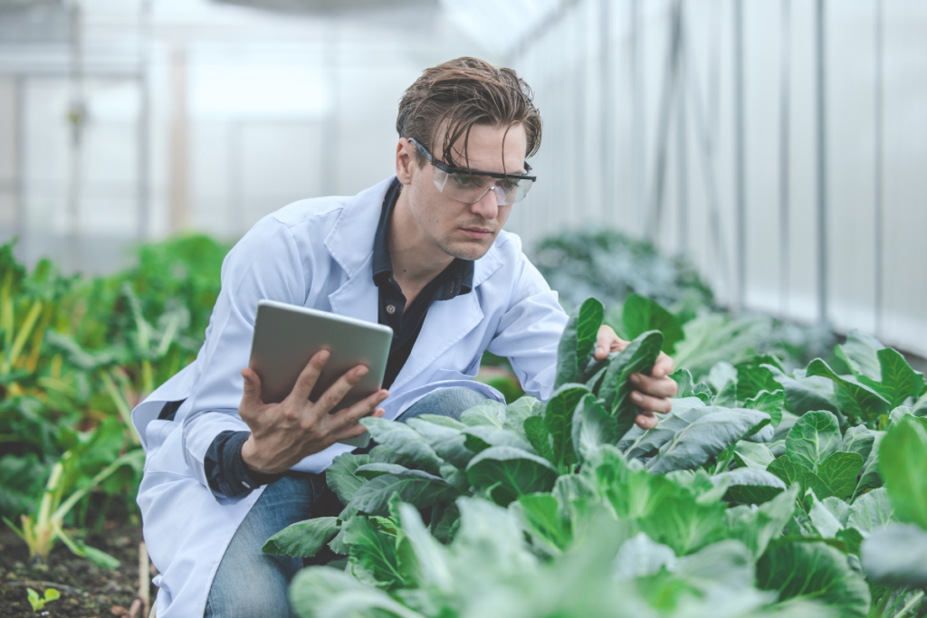 A person in a white coat holding a tablet in a greenhouse. Invest in Holland.