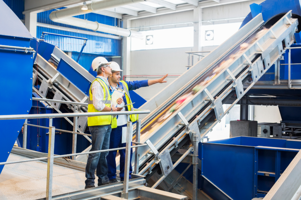 Two people in safety vests standing near a conveyor belt. Invest in Holland.